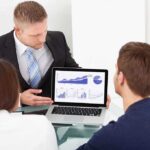 Business professional presenting data on a laptop to two colleagues